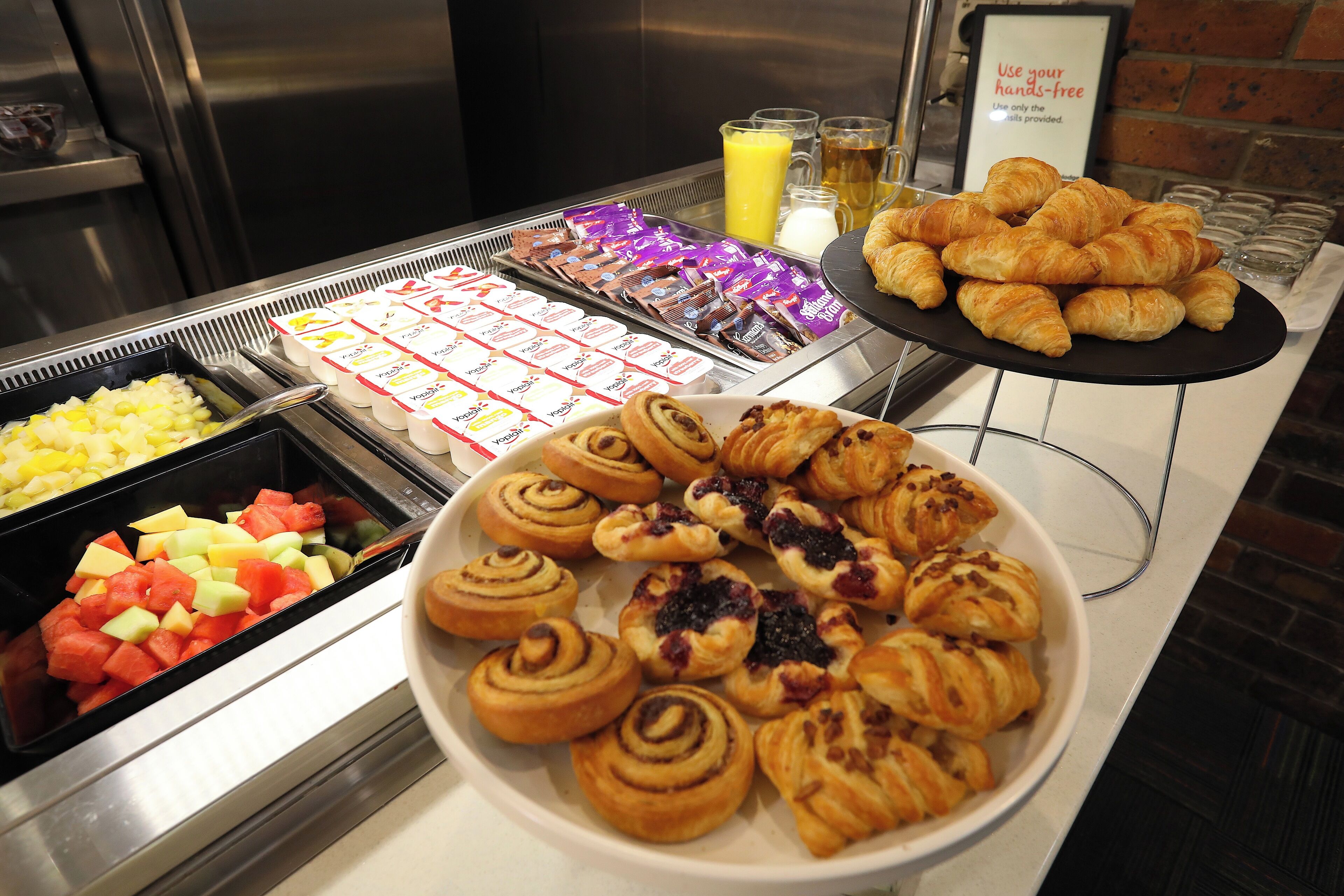 En buffet med et udvalg af madvarer, herunder frugt, bagværk og drikkevarer.