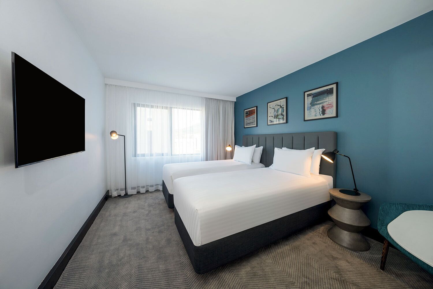 Quarto de hotel com uma cama grande, televisão de tela plana, mesa de cabeceira e janela com cortinas.