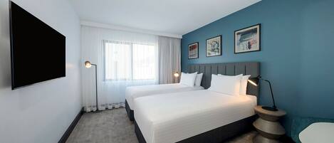 Quarto de hotel com uma cama grande, televisão de tela plana, mesa de cabeceira e janela com cortinas.