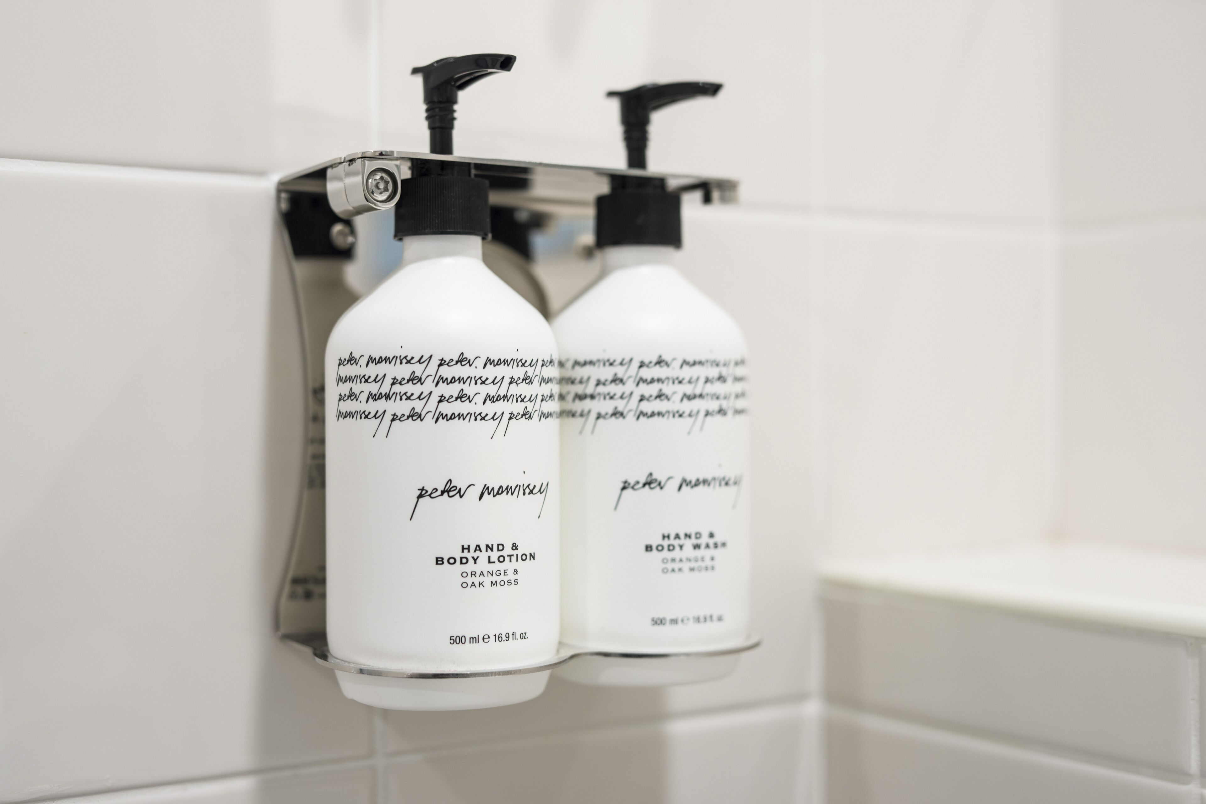 Twee flessen hand- en bodylotion van Peter Monisey aan een muur bevestigd.