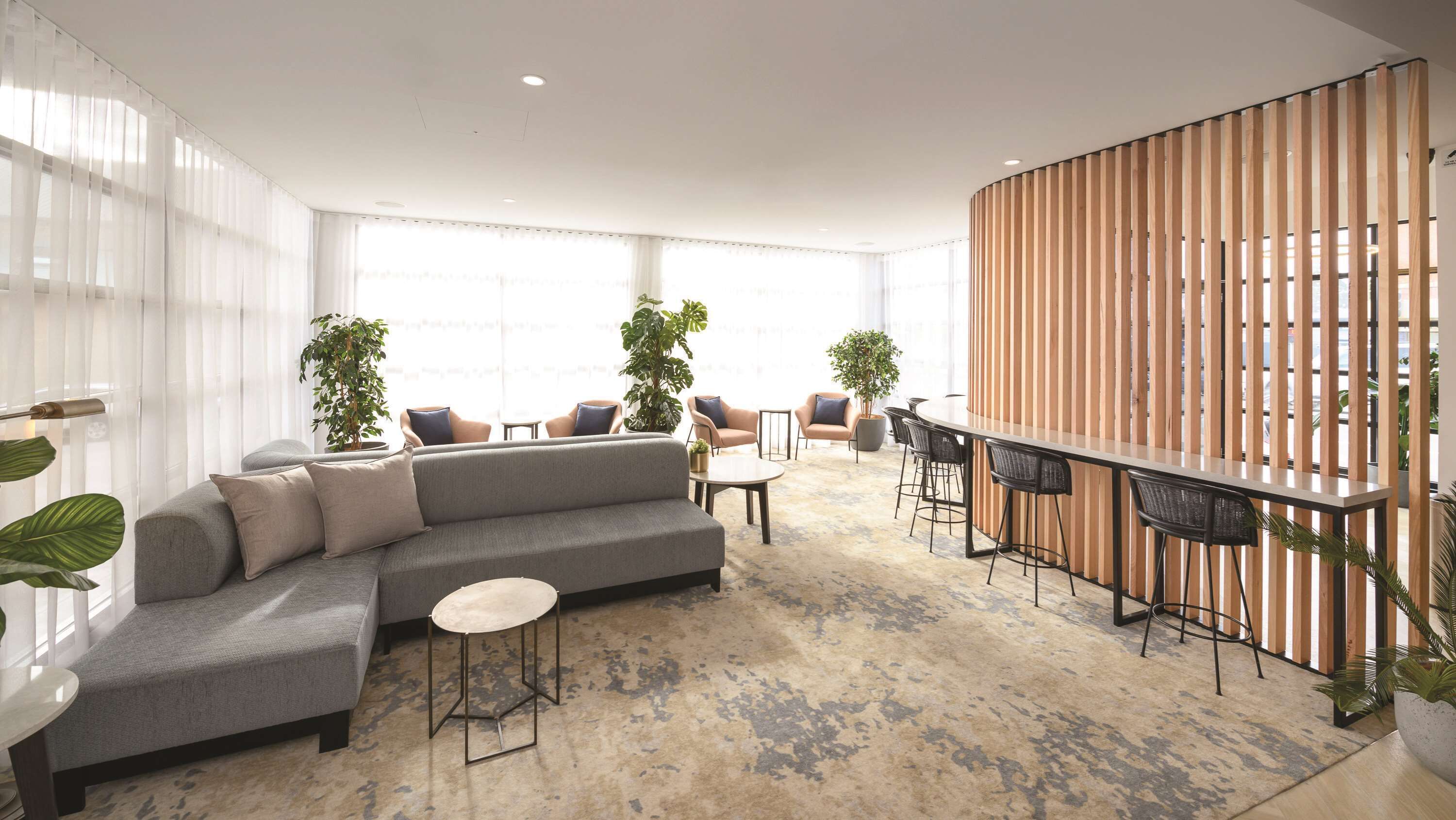 A modern lounge area with a grey sectional sofa, round tables, and bar seating.
