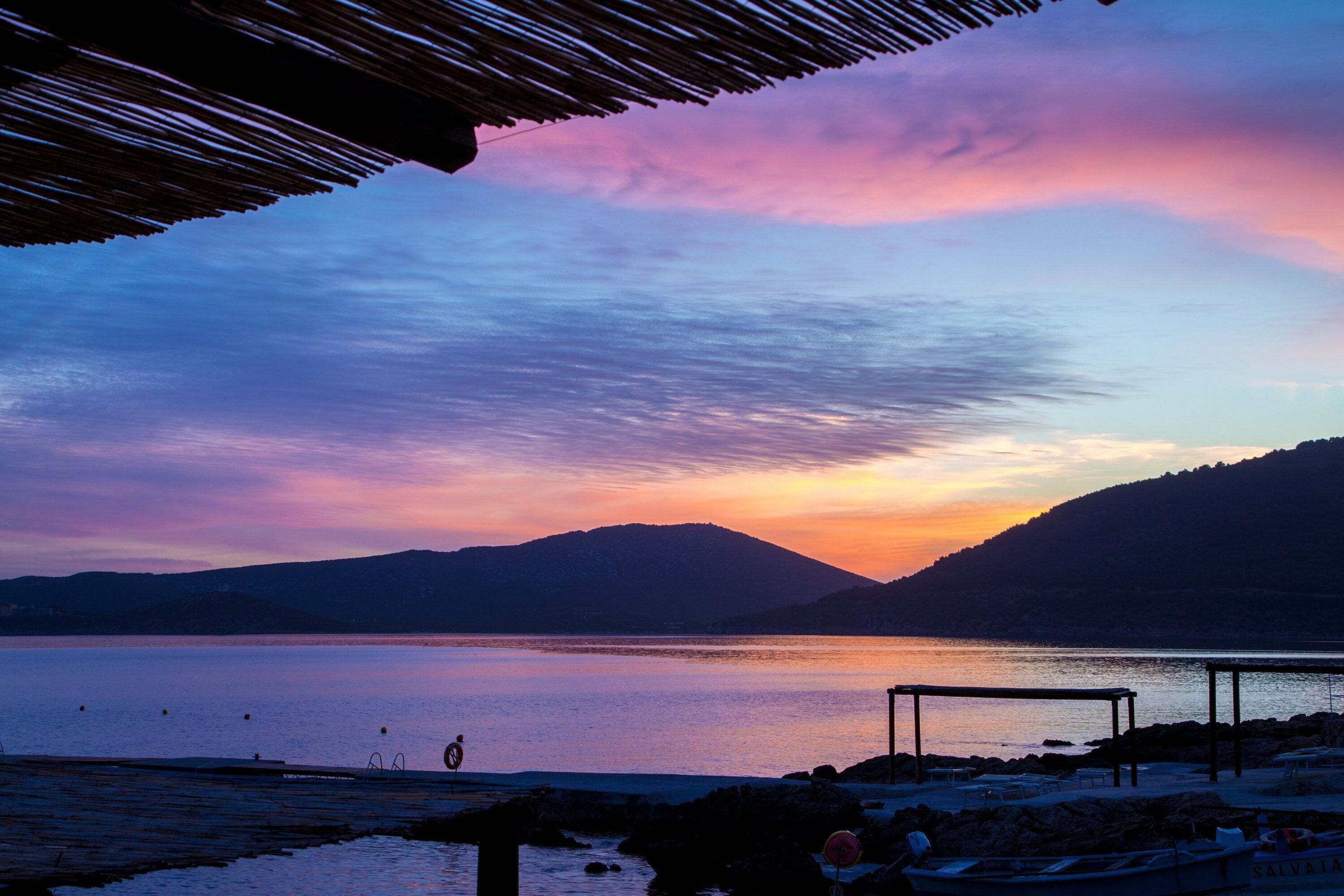 Vista del lago con un atardecer, montañas al fondo y un pabellón con vistas al agua.