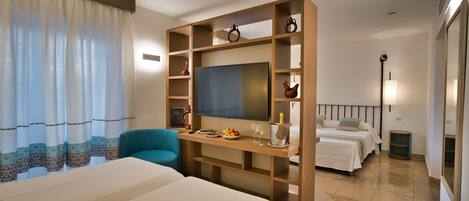 A hotel room with a large bed, a desk with a TV, a chair, and a small table with a bottle and glasses.