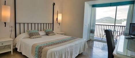 A bedroom with a bed, bedside tables, a desk, and a balcony with a view.