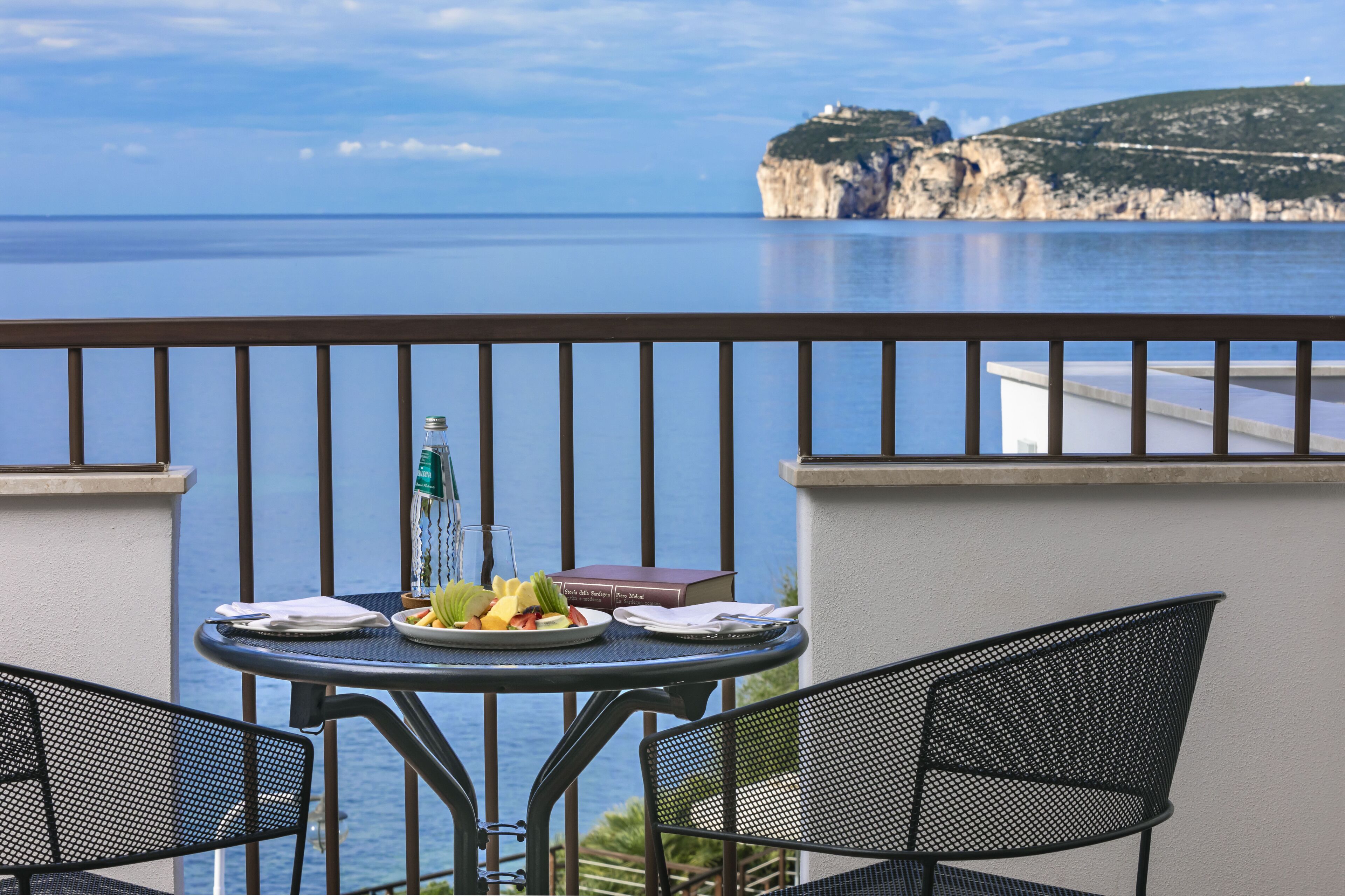 A balcony with a table set for two, overlooking a coastal view with cliffs.