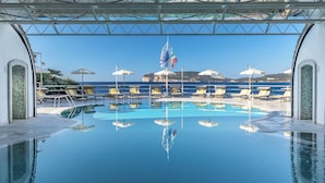 Un espace piscine avec une eau d’un bleu limpide, des chaises longues, des parasols et des drapeaux.