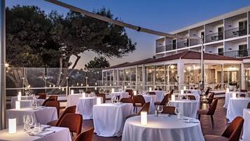 An outdoor dining area with round tables, white tablecloths, and candle centerpieces.