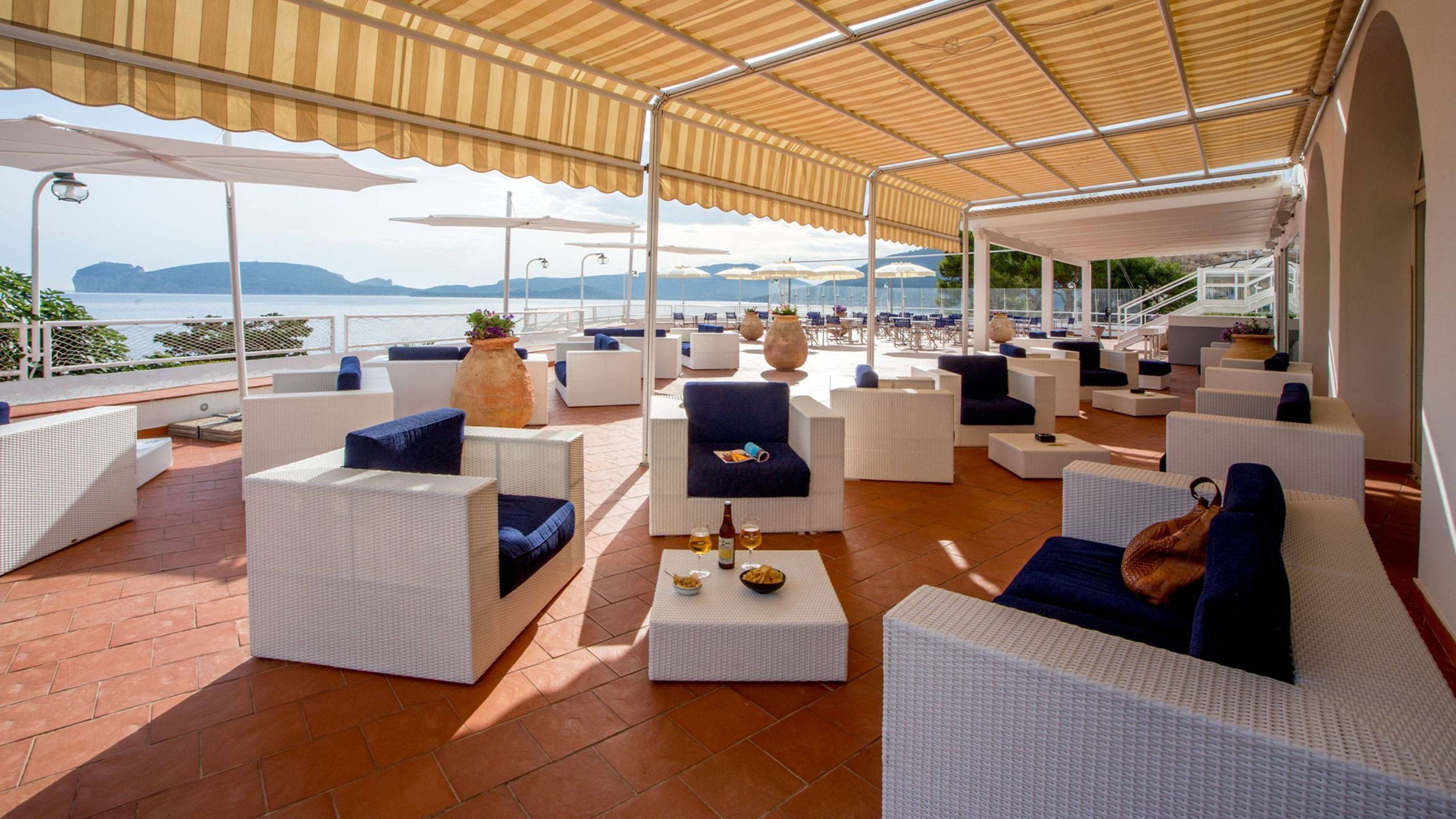 A covered outdoor seating area with white wicker furniture and blue cushions, overlooking a scenic view.