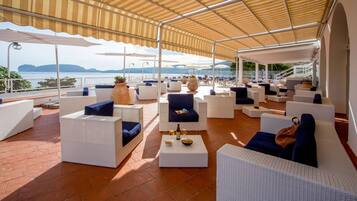 A covered outdoor seating area with white wicker furniture and blue cushions, overlooking a scenic view.