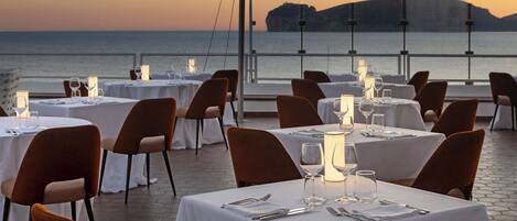 A restaurant with tables set for dining, overlooking a body of water and a distant landform.