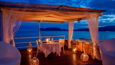 An outdoor dining area with a table set for two, overlooking a body of water.