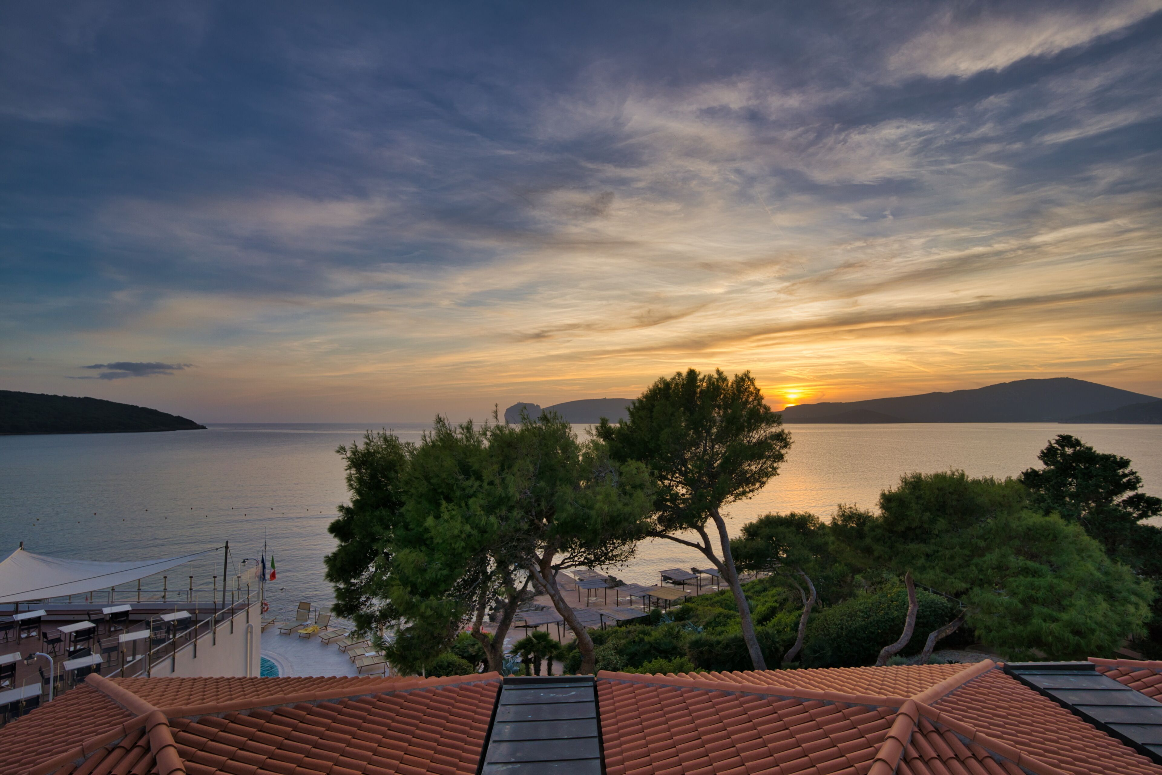 Une vue sur la côte, avec un coucher de soleil sur l’eau, des arbres et un toit recouvert de tuiles.