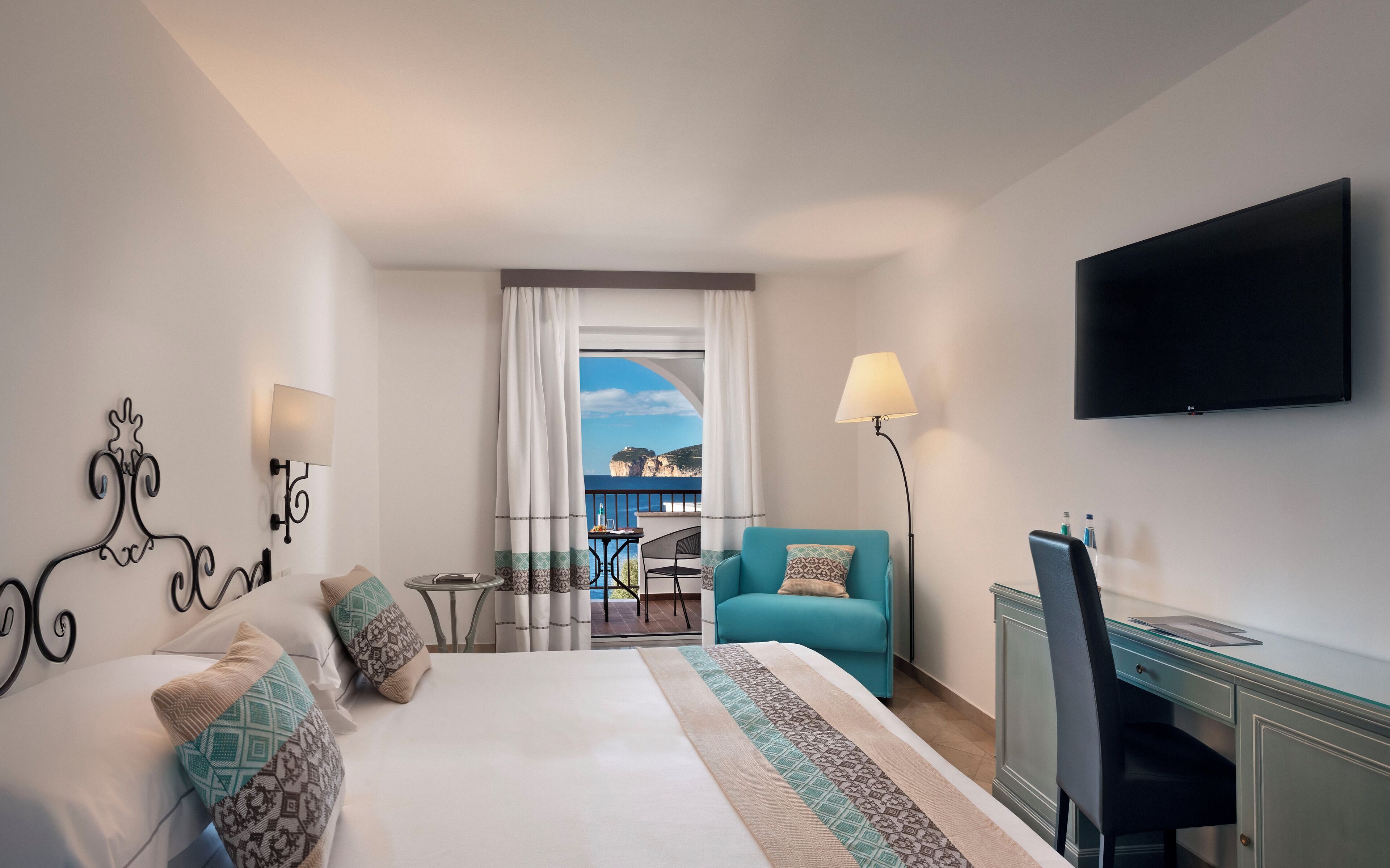 Een hotelkamer met een bed, een bureau, een stoel, een televisie en uitzicht op zee.