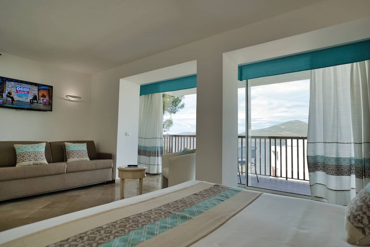 Una habitación de hotel con cama, sofá, televisión, balcón y vistas al mar, además de una pequeña mesa.