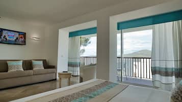 Una camera d'albergo con un letto, un divano, una TV, un balcone vista mare e un tavolino.