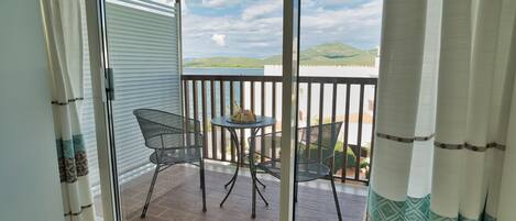 Un balcone con tavolo e sedie, vista sul mare e una montagna sullo sfondo.