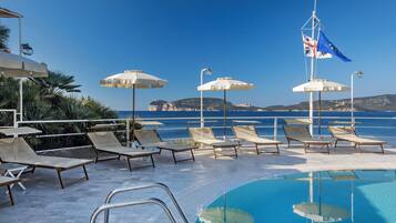 A pool area with lounge chairs and umbrellas, a flag, and a view of the sea.