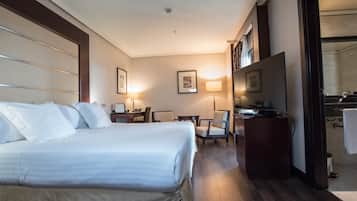 Habitación de hotel con una cama grande, un escritorio con silla, televisión y baño visible a través de una puerta abierta.