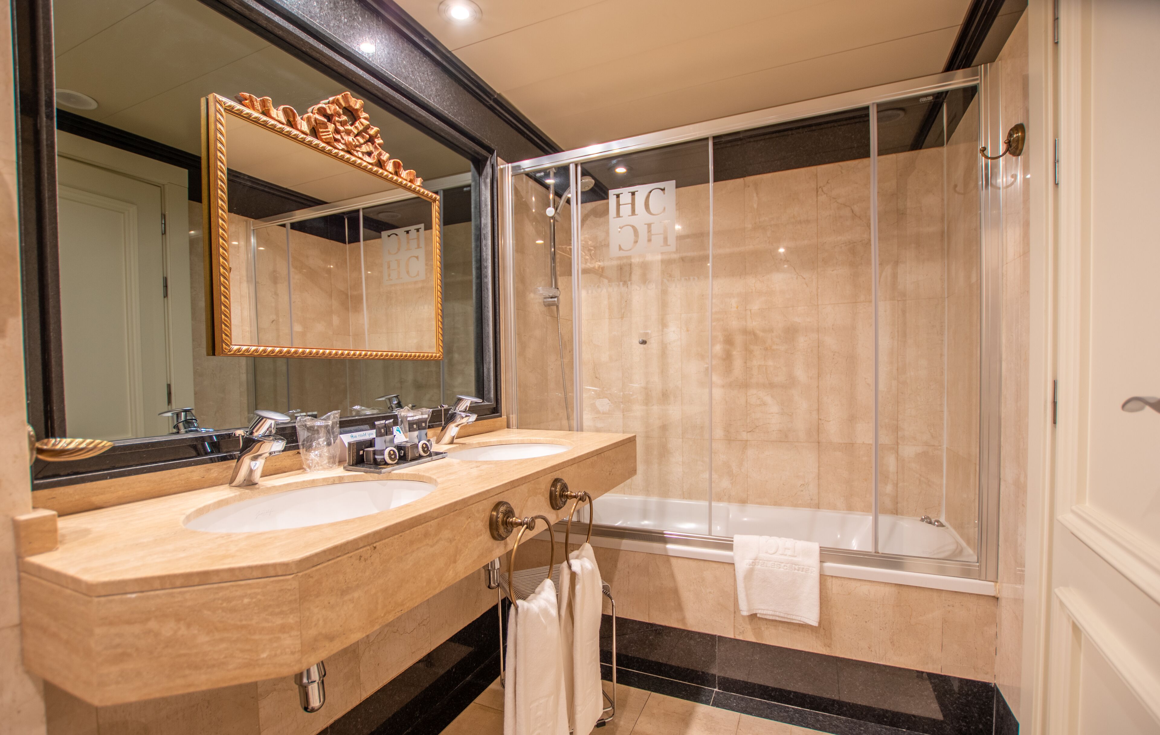 A modern bathroom with two sinks, a large mirror, and a glass-enclosed shower area.