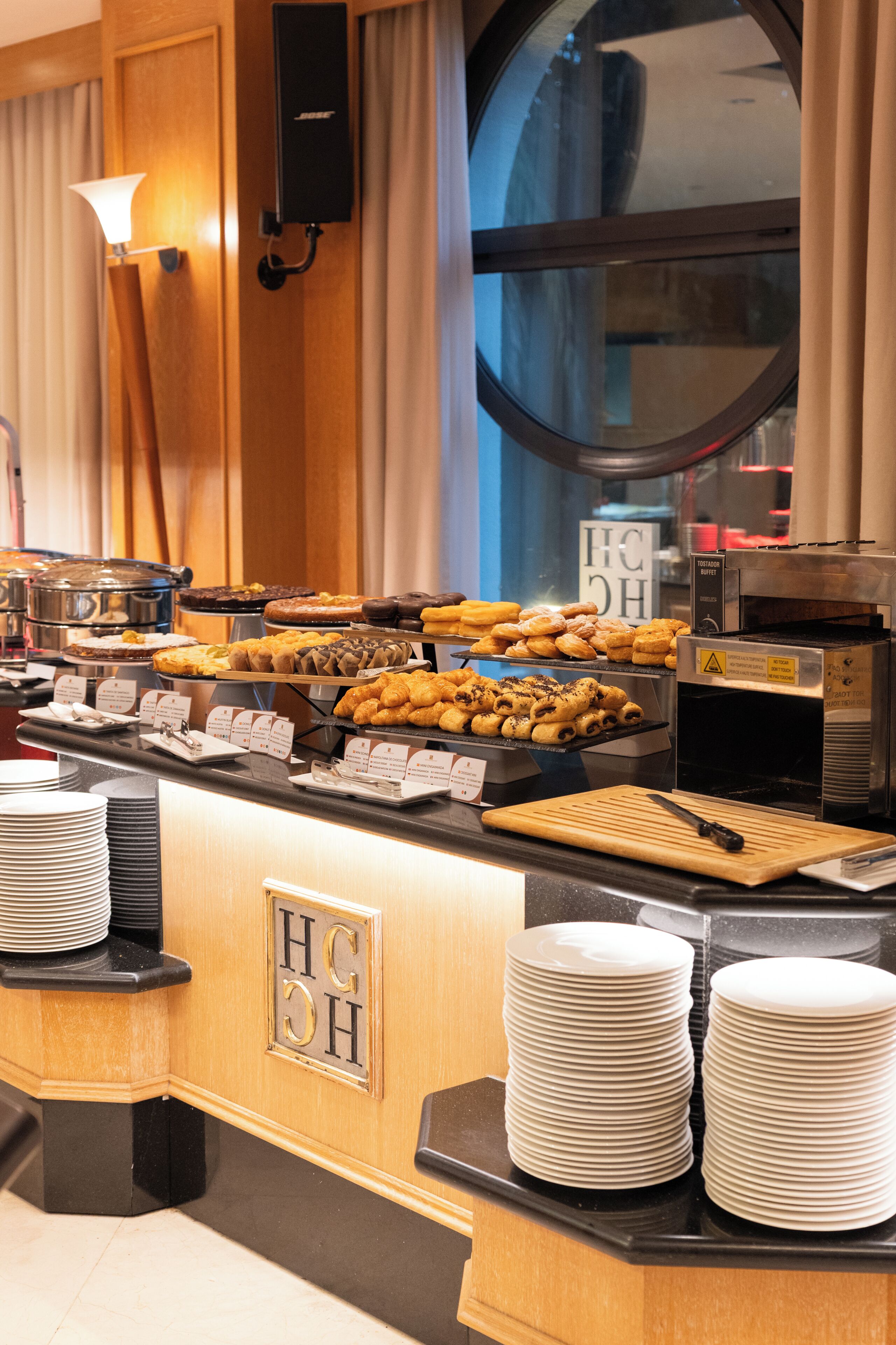 A buffet counter with various food items, a coffee machine, and stacks of white plates.