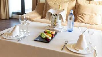 Una mesa de comedor dispuesta con platos blancos, cubiertos y copas, junto con una bandeja de frutas y una botella de champán.