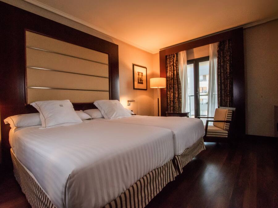 Camera d'albergo con un ampio letto, una poltrona, una scrivania e una televisione.