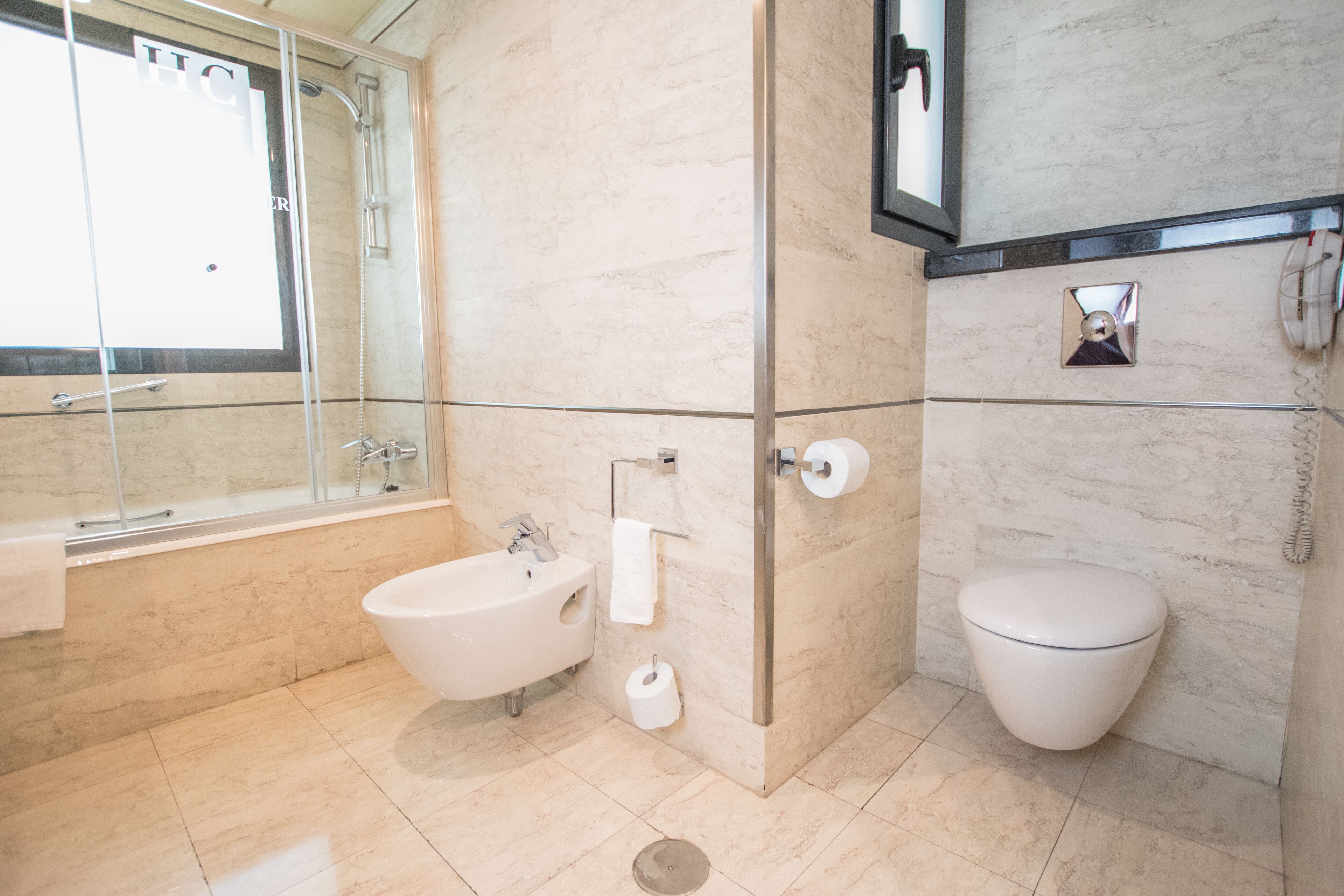 A modern bathroom with a bathtub, bidet, toilet, and a glass-enclosed shower area.
