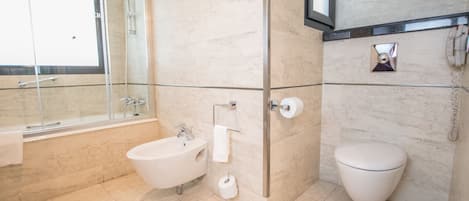 Et moderne badeværelse med badekar, bidet, toilet og en bruseafskærmning i glas.