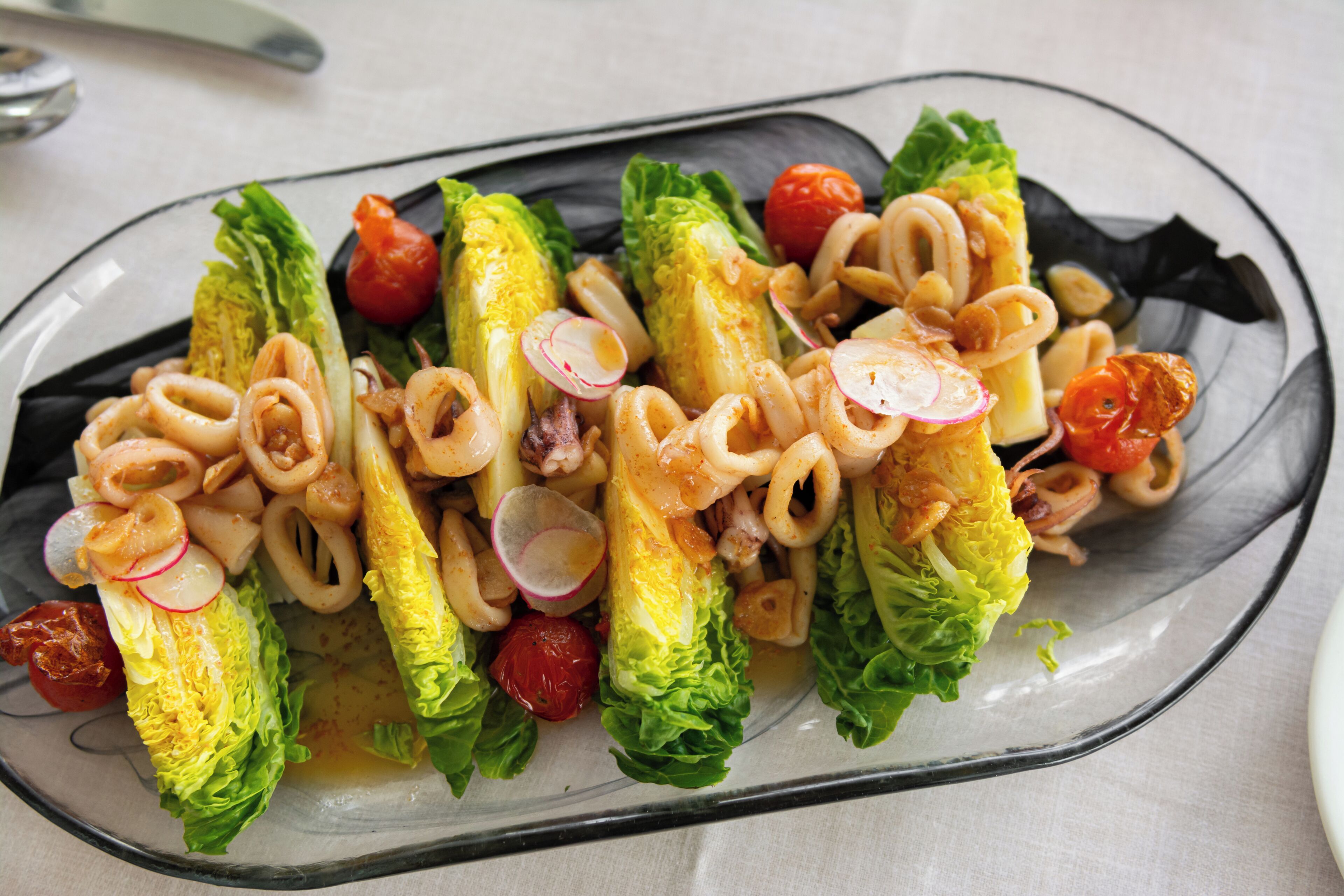 Une salade composée de laitue, de tomates et de tentacules de poulpe, servie dans une assiette en verre.