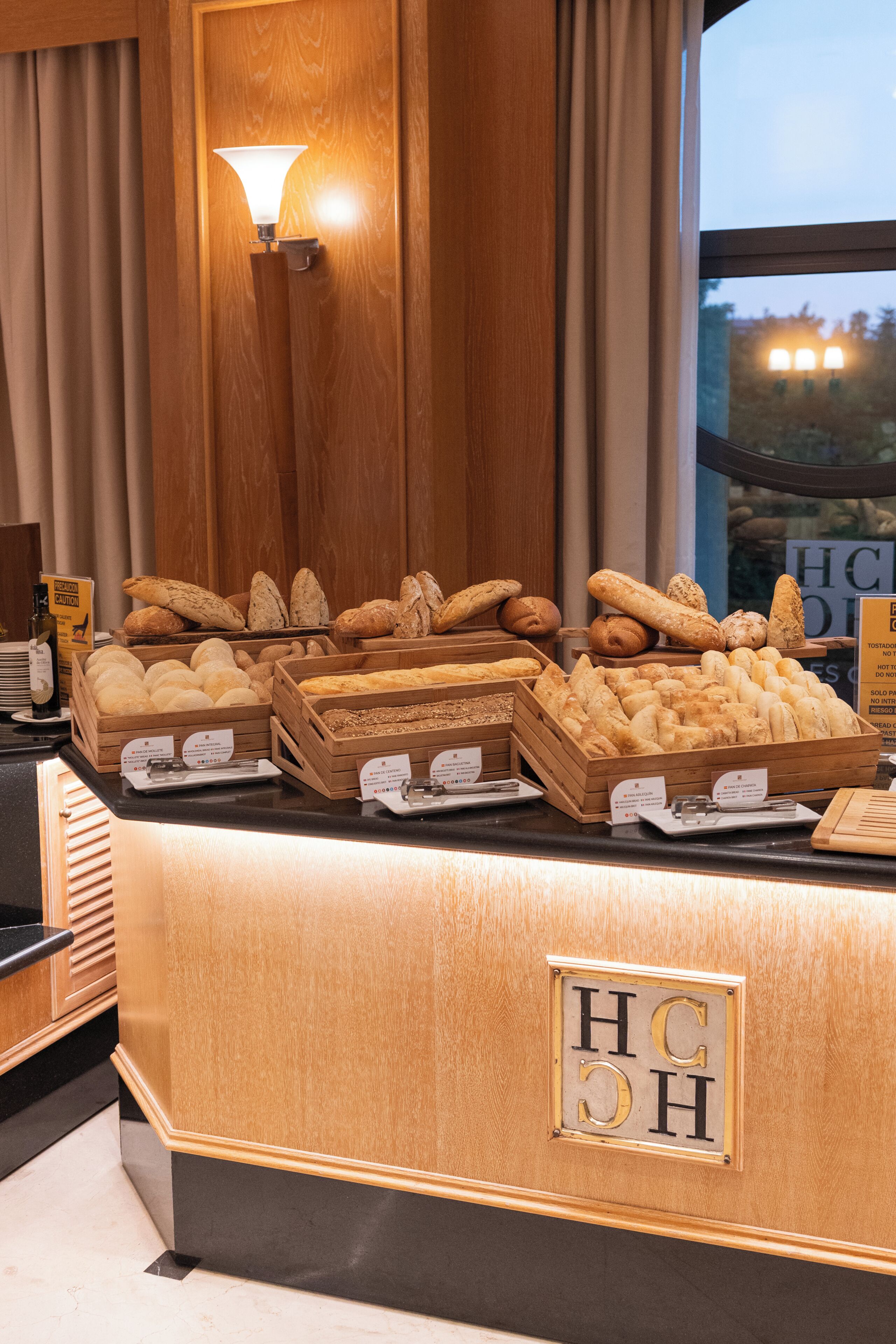 A bakery display with various breads and pastries, a wooden counter, and a sign with 'HC' letters.