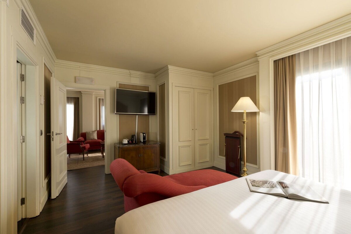 Una habitación de hotel con una cama, un escritorio, un televisor, una lámpara y una silla roja.