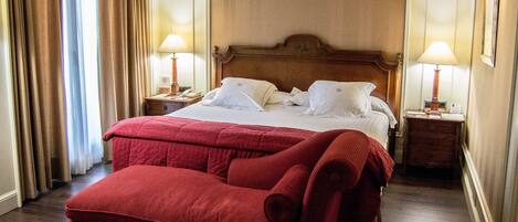 A hotel room with a large bed, two bedside tables with lamps, a red sofa, and curtains.