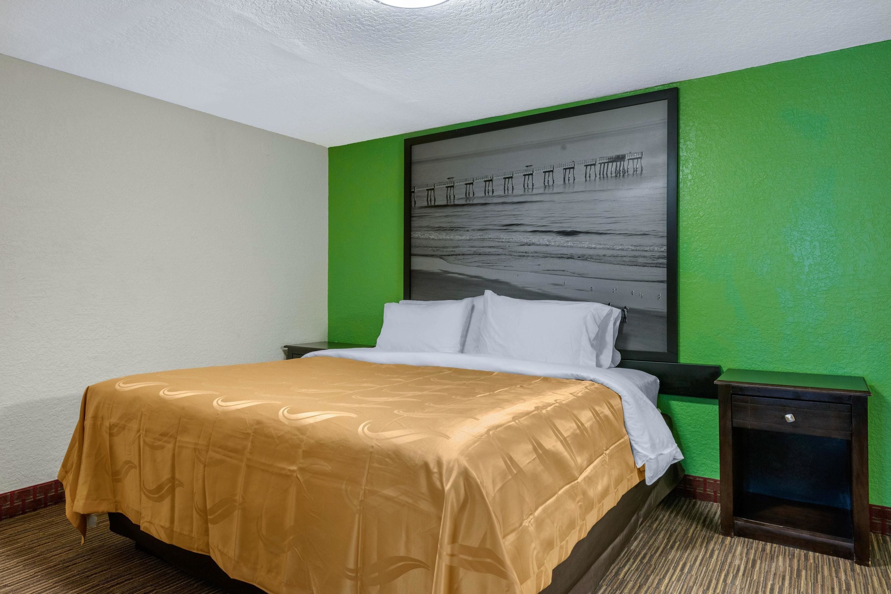 Ein Hotelzimmer mit Bett, grünen Wänden, einem großen gerahmten Bild an der Wand und einem Nachttisch.