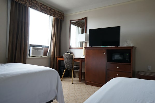 A hotel room with two beds, a desk with a chair, a television, a microwave, and a large window with curtains. - The Prince Arthur Hotel (Thunder Bay)