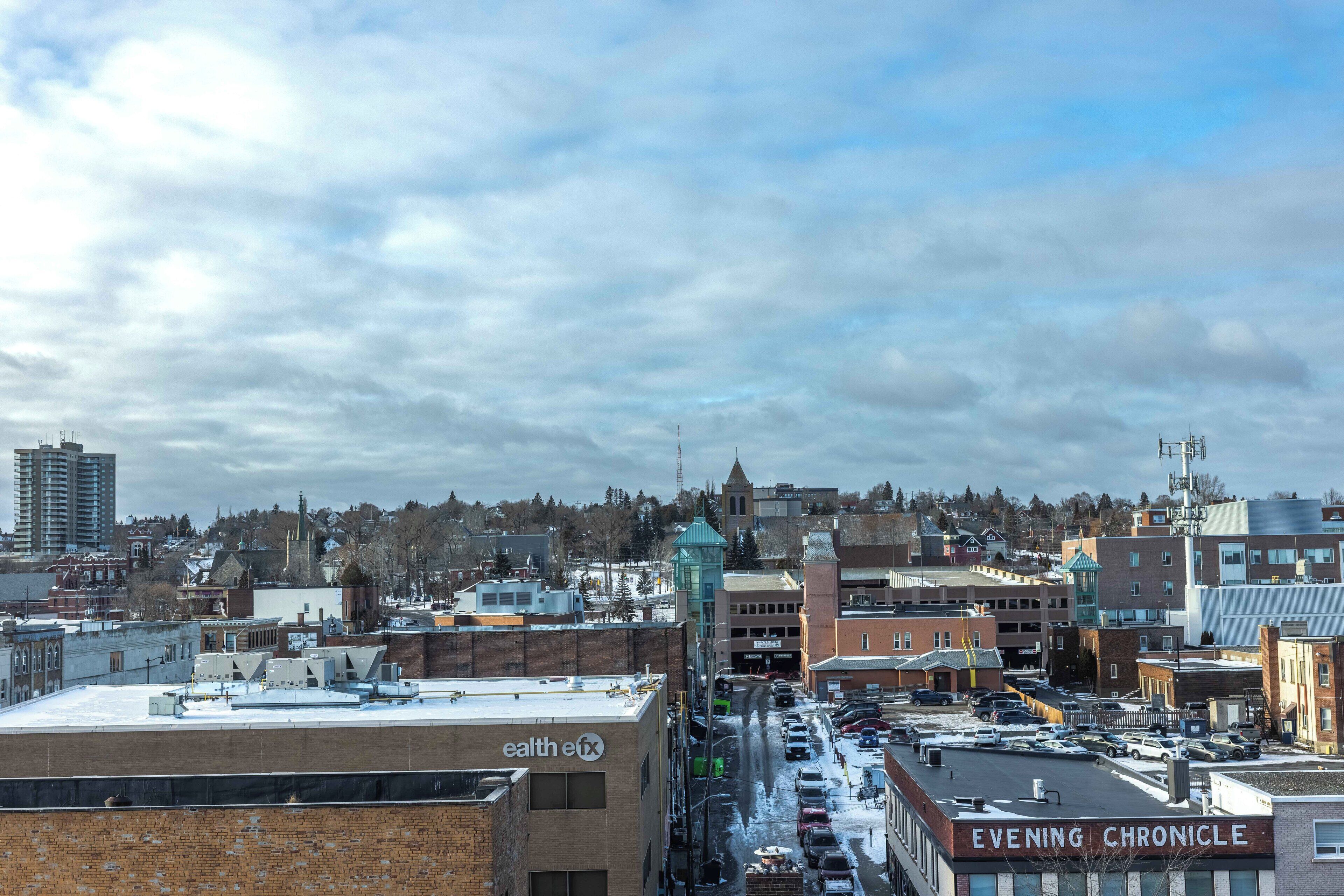 A cityscape with a parking lot, buildings, and a cloudy sky.