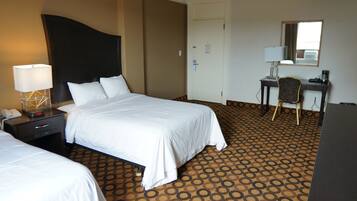 A hotel room with a large bed, a desk, a chair, and a desk lamp.