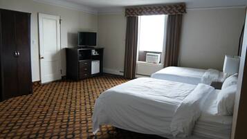 A hotel room with two beds, a TV, a desk, and a window with curtains.