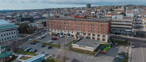 Un edificio grande con varios pisos, un estacionamiento con varios autos y un puente peatonal.