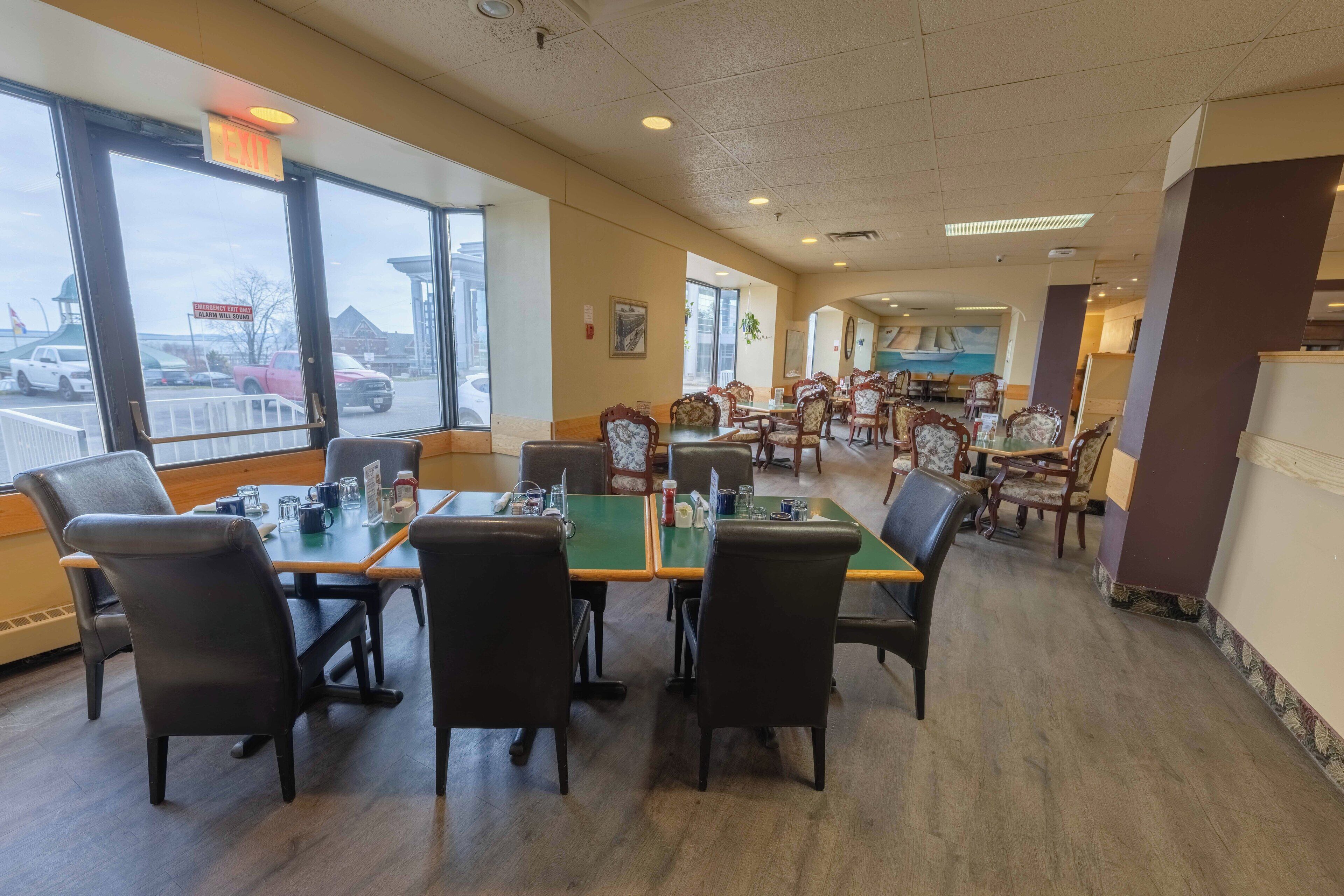 Un restaurante con una barra larga y varias mesas, ventanas amplias y vista al estacionamiento.