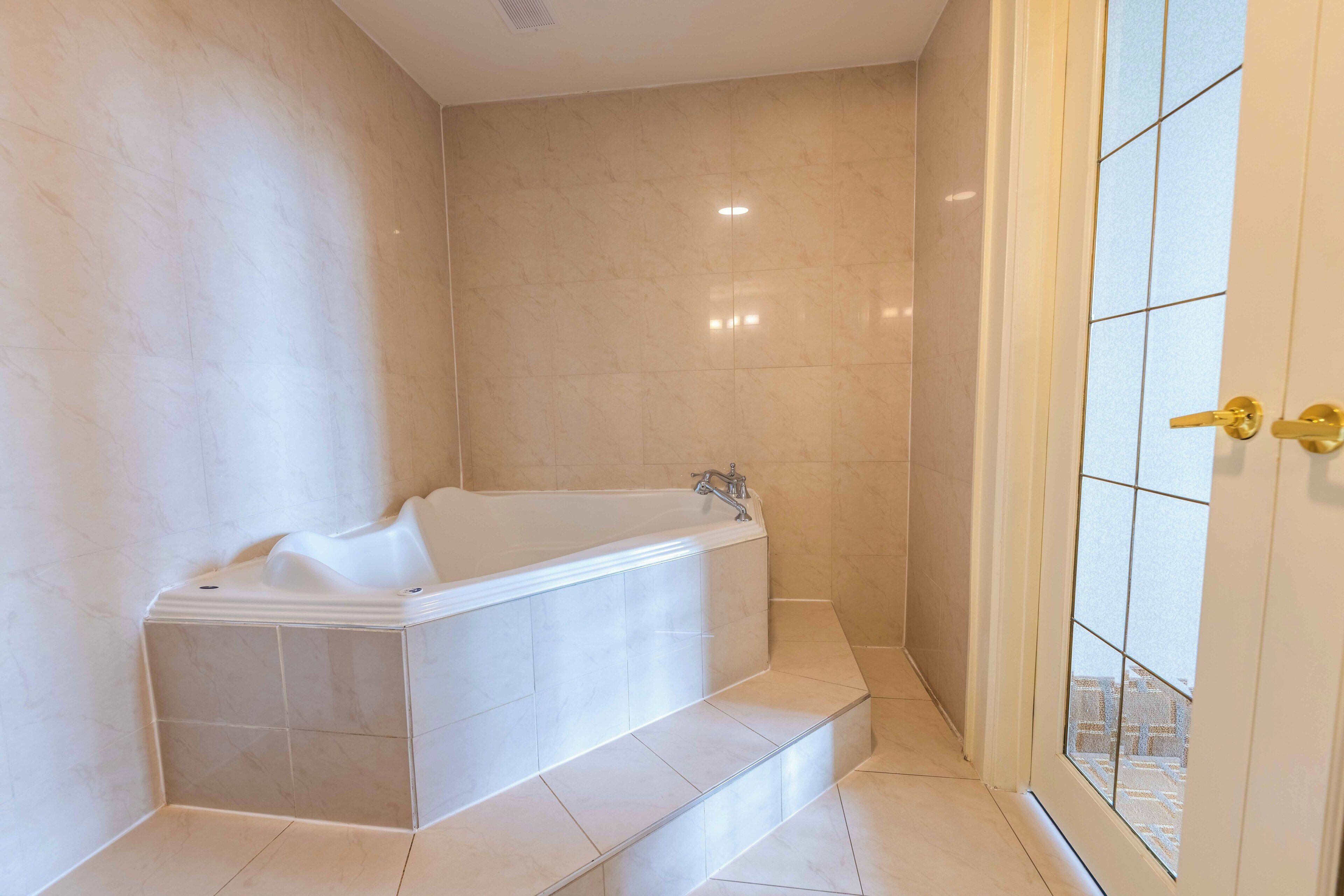 A modern bathroom with a freestanding bathtub, tiled walls, and a glass door leading to an outdoor area.