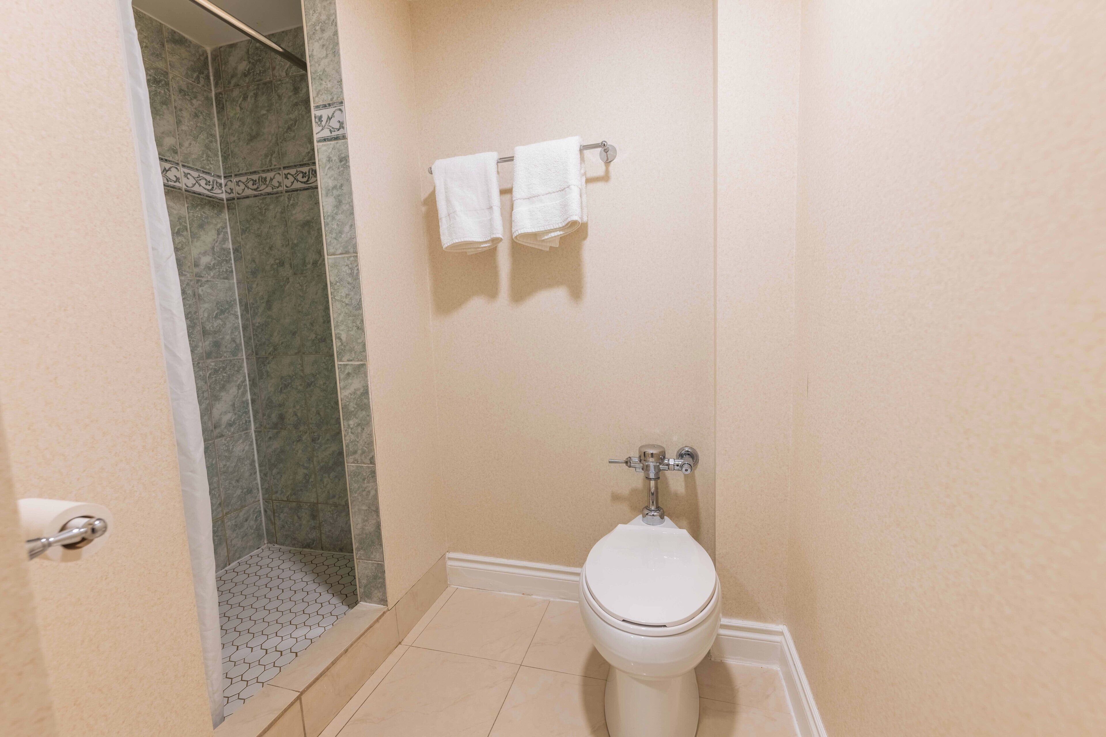 Un baño con inodoro, ducha con pared de azulejos y un perchero con dos toallas.