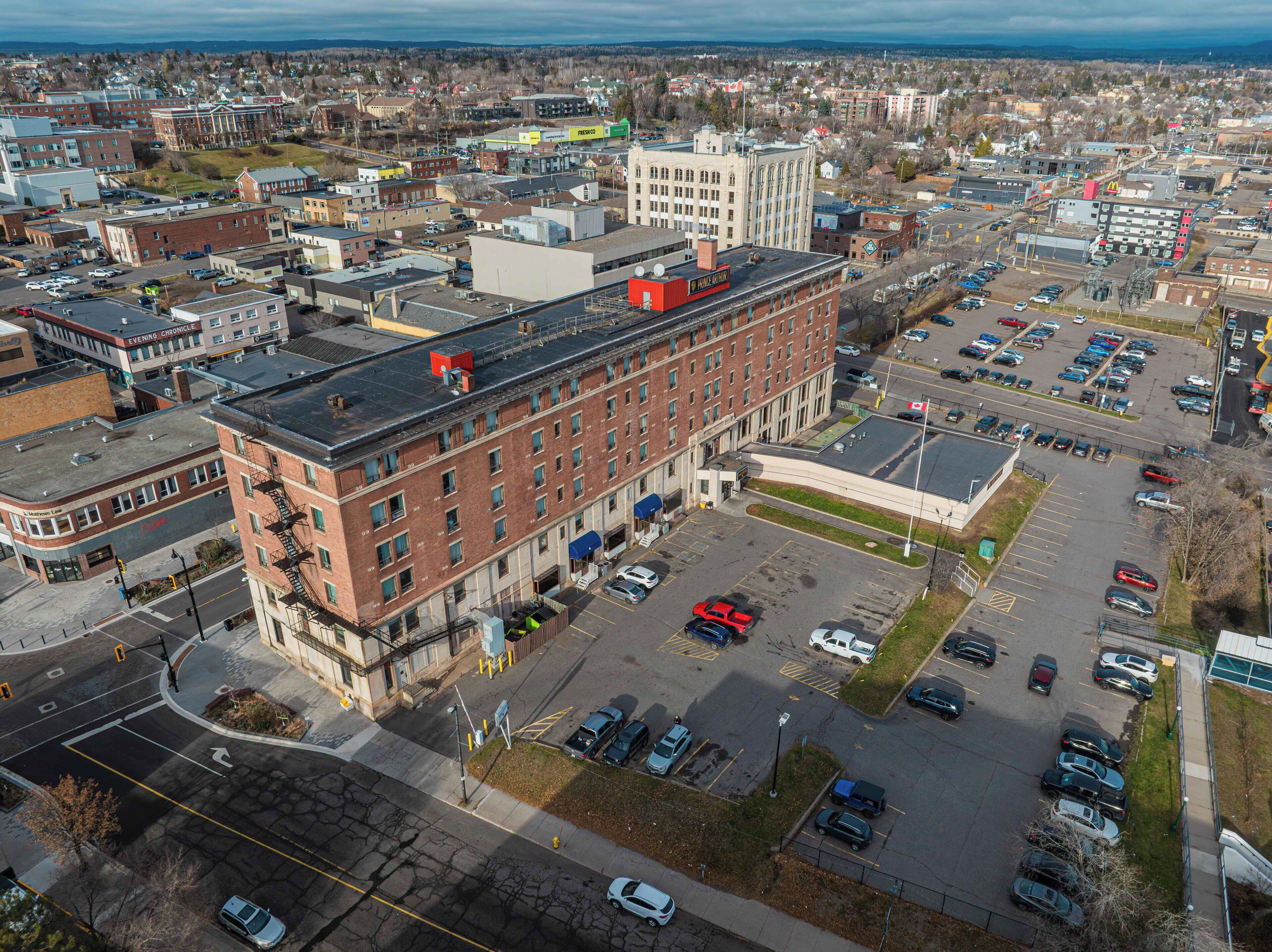 An aerial view of a cityscape with a prominent red-brick building with multiple windows and a flat roof.
