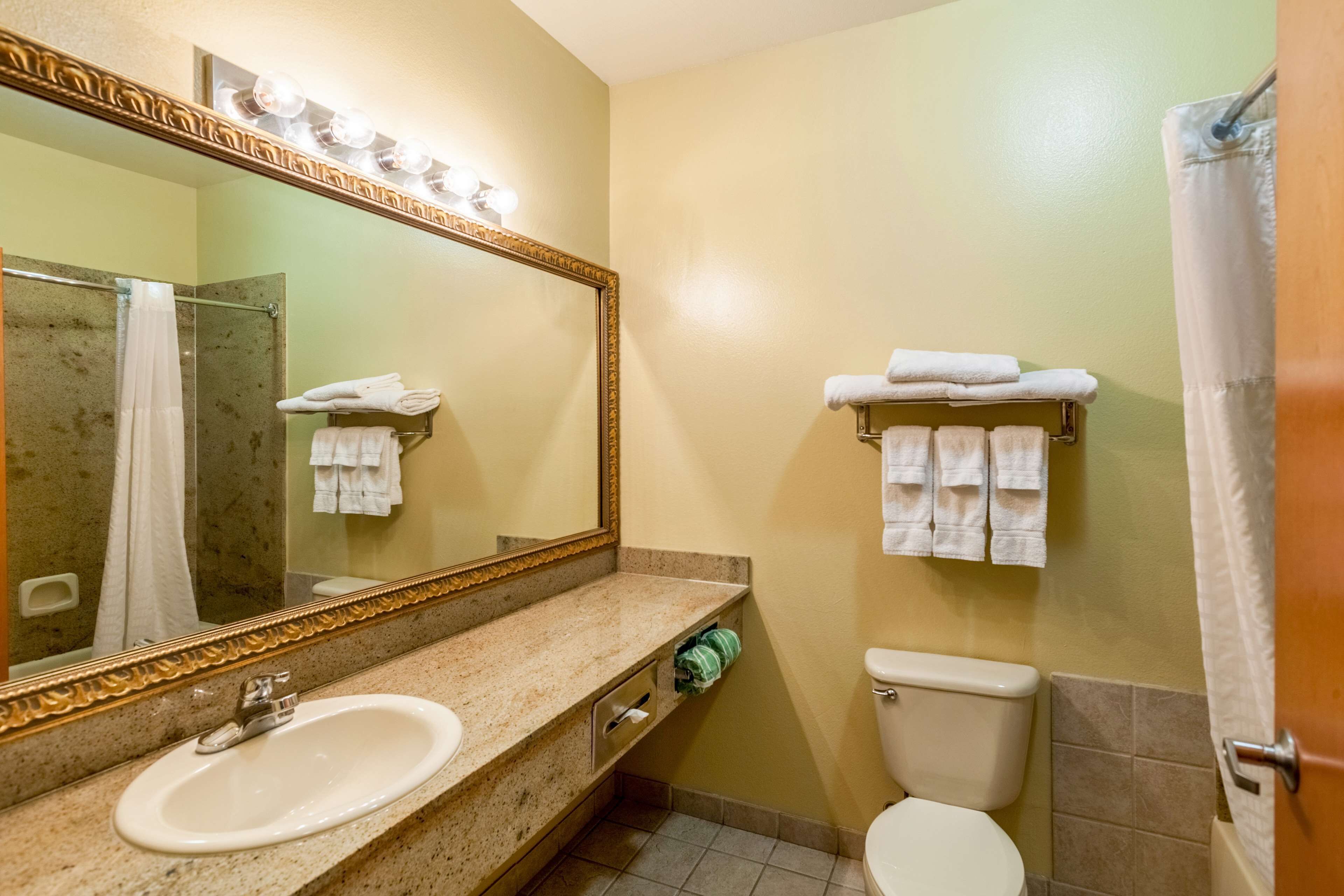 A bathroom with a sink, mirror, and toilet. There are towels on the wall and in a rack.