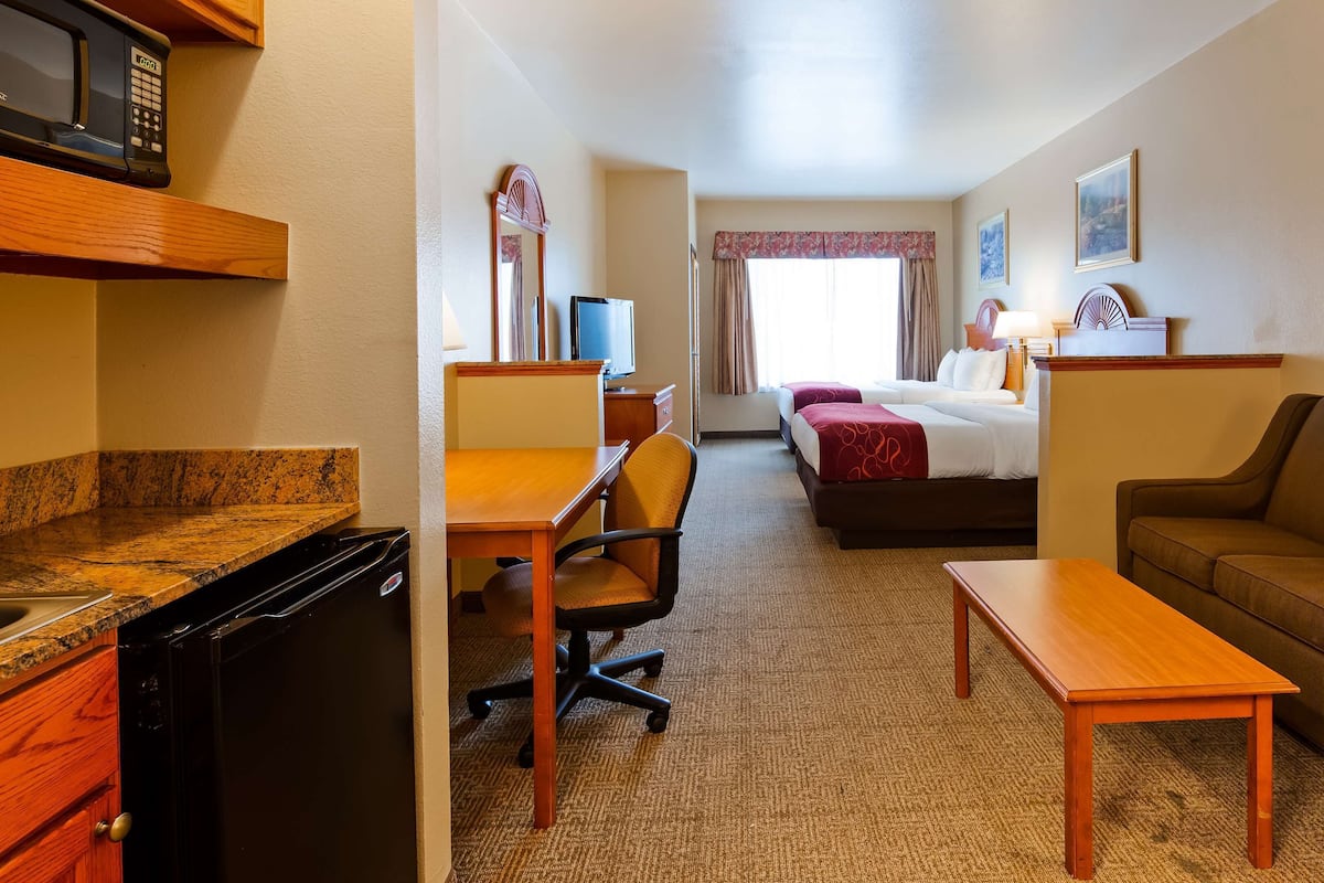A hotel room with a kitchenette, a dining area, a sofa, a bed, and a window with curtains.