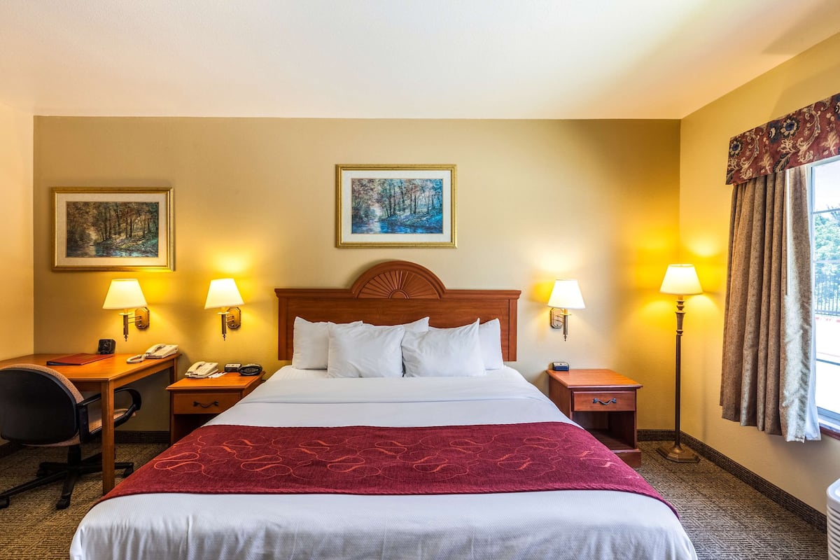 A hotel room with a large bed, two bedside tables with lamps, a desk with a chair, and two framed pictures on the wall.