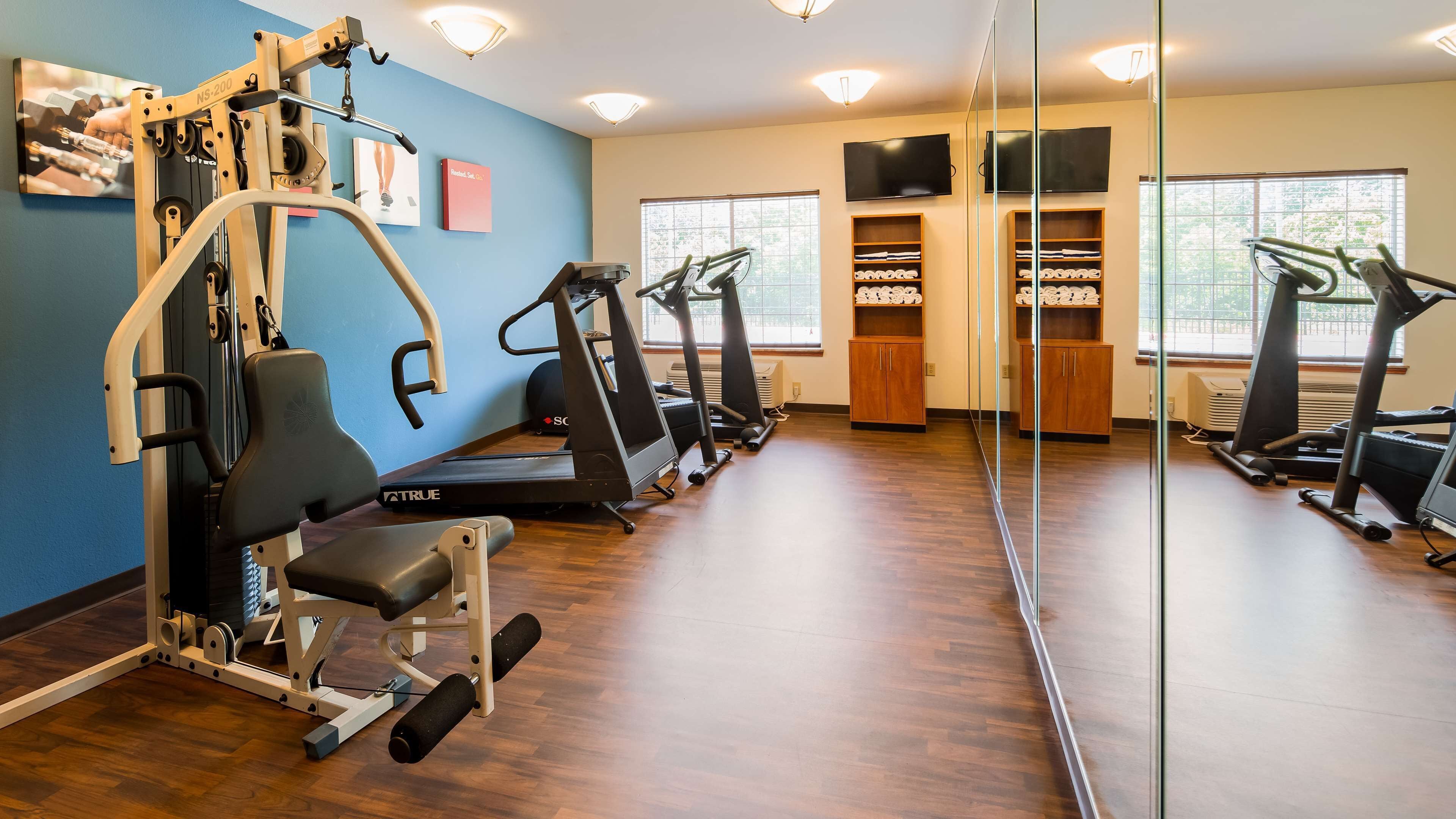 A gym with exercise equipment, a mirrored wall, and a TV on the wall.