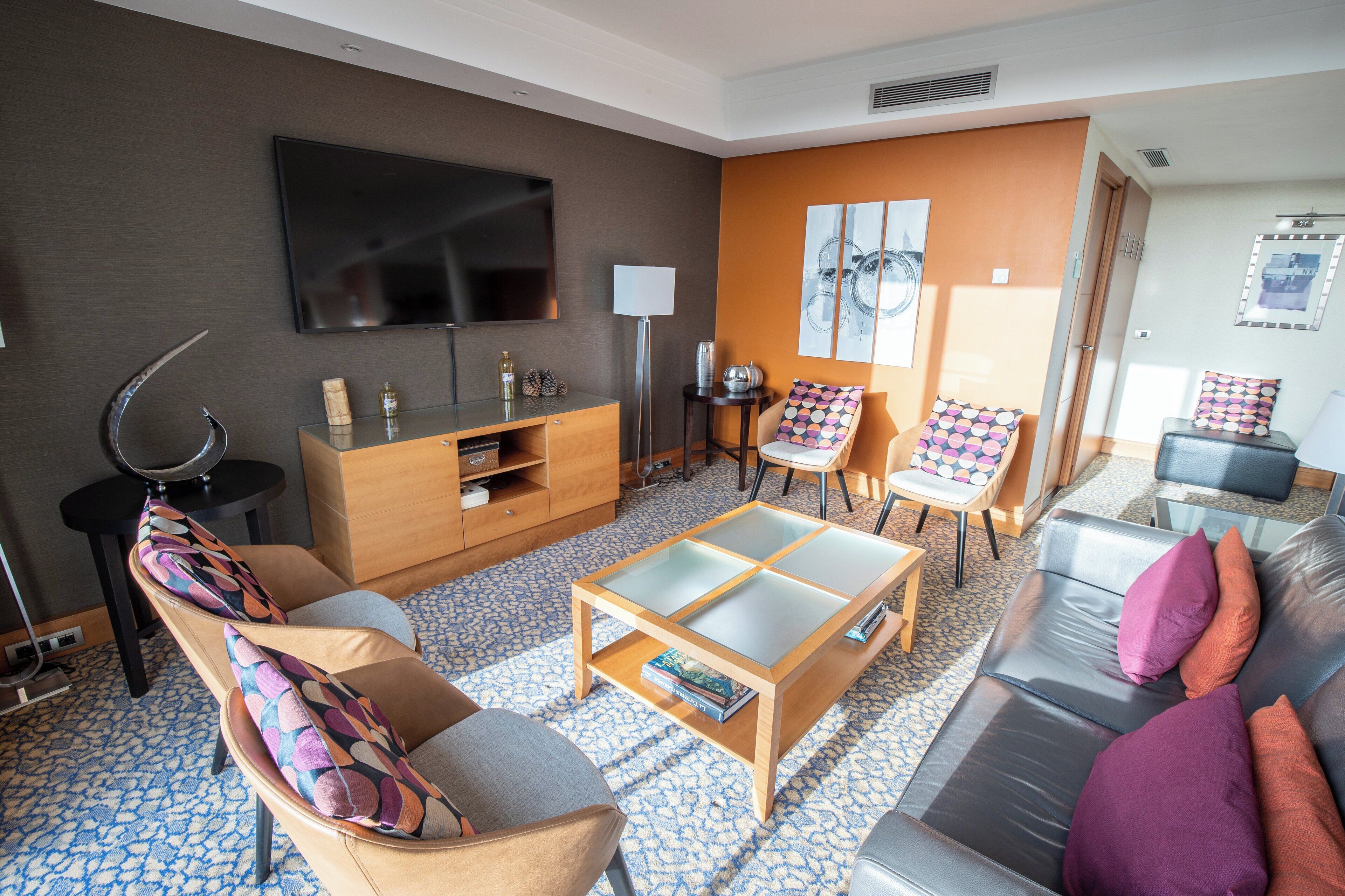 Una sala de estar moderna con un sofá, un sillón, una mesita de centro y un televisor montado en la pared.