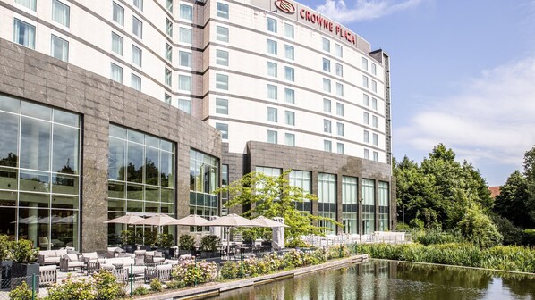 Ein Hotel mit großer Glasfassade, Außenbereich mit Sonnenschirmen und einem Teich davor.