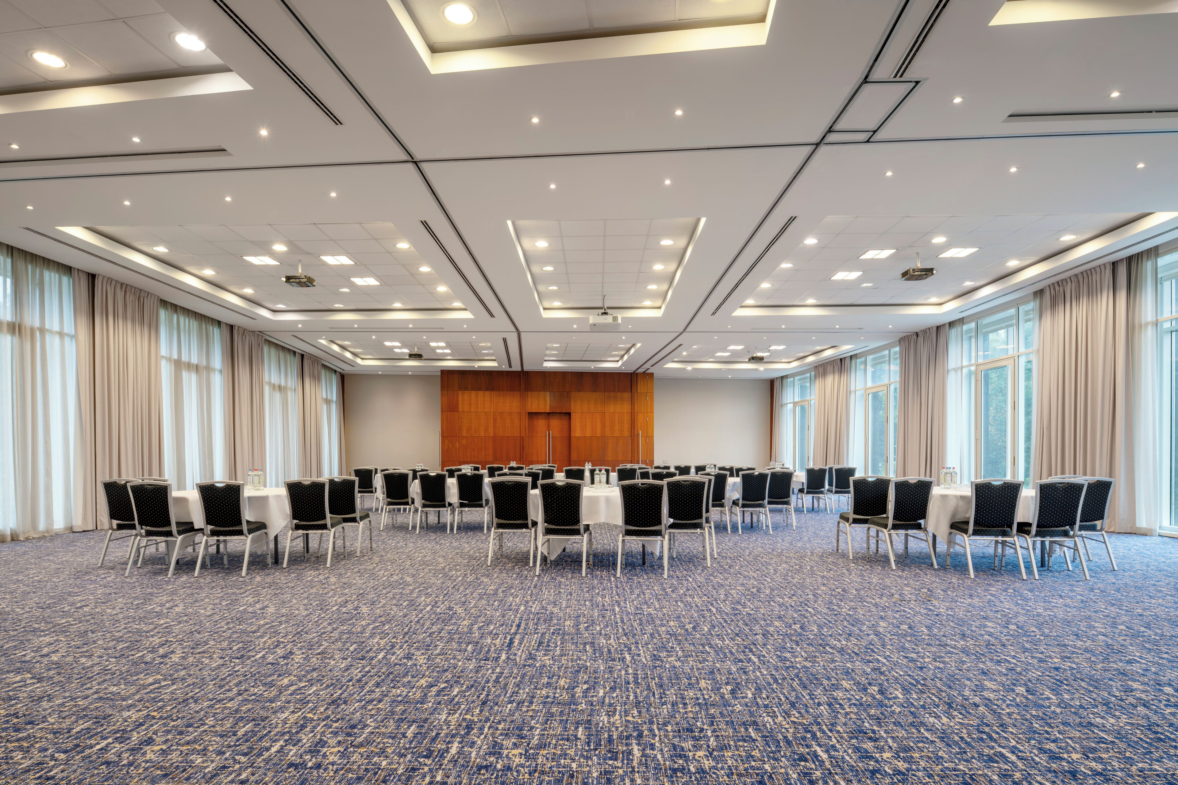 Un salón de conferencias con filas de sillas, un escenario con atril y ventanas amplias.