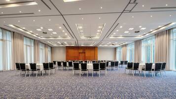 Un salón de conferencias con filas de sillas, un escenario con atril y ventanas amplias.